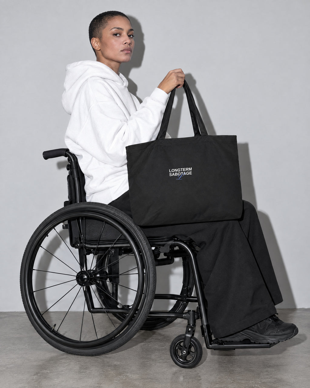 LONGTERM SABOTAGE Large Tote, Black, on the lap, wheelchair, profile, grey studio